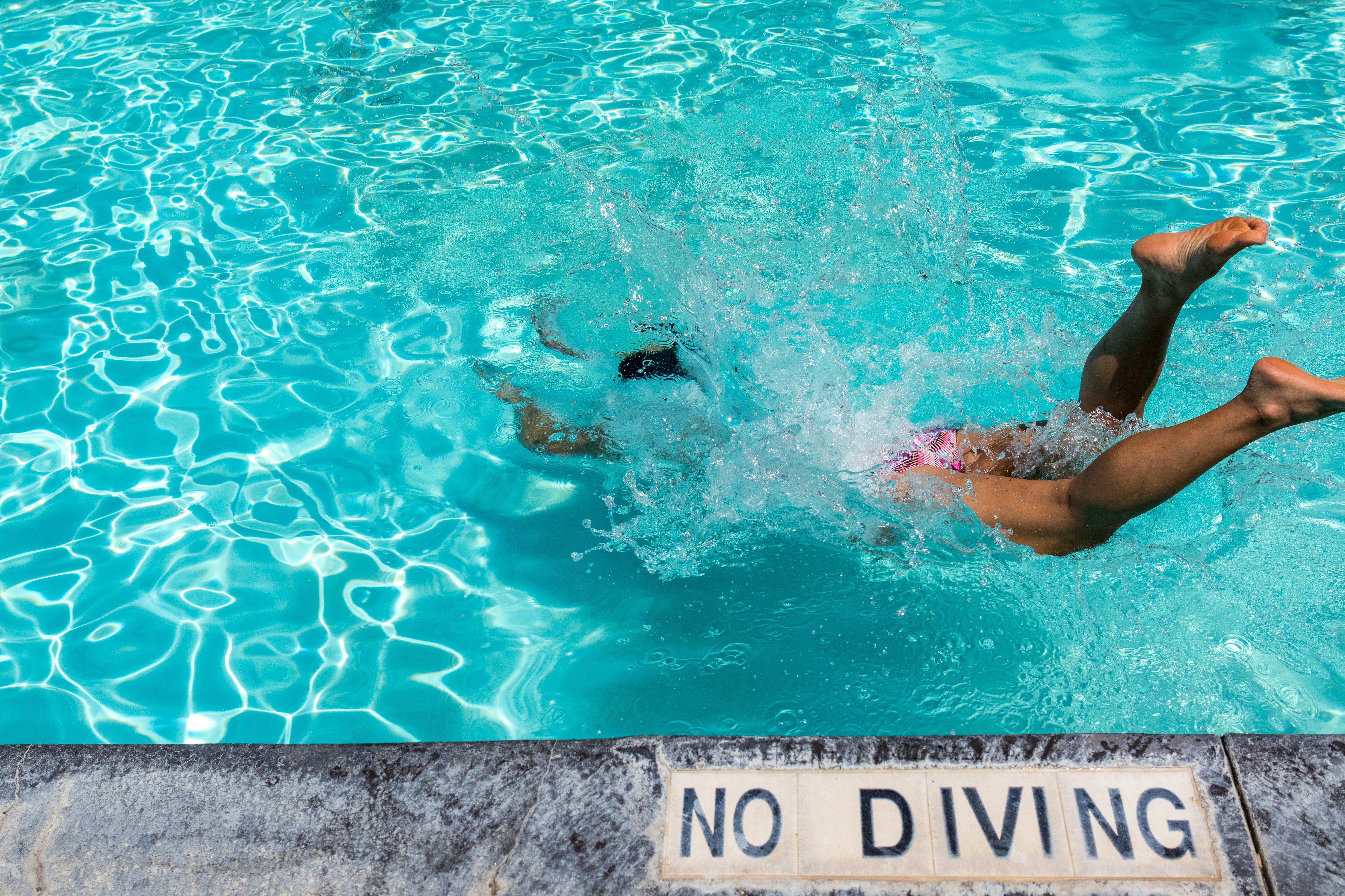 person diving on pool during daytime